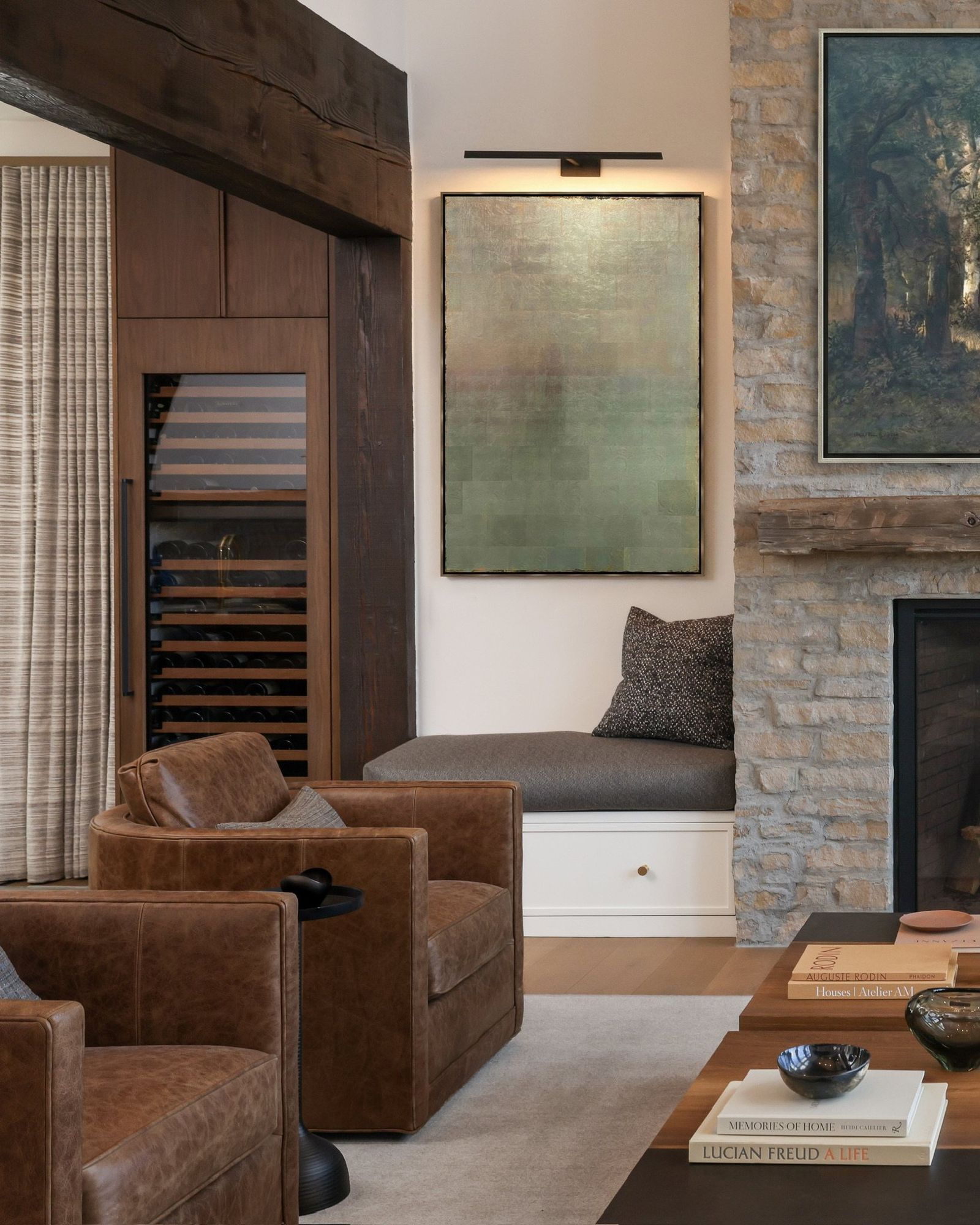 Leather club chairs by a window seat and stone fireplace wall with a landscape painting