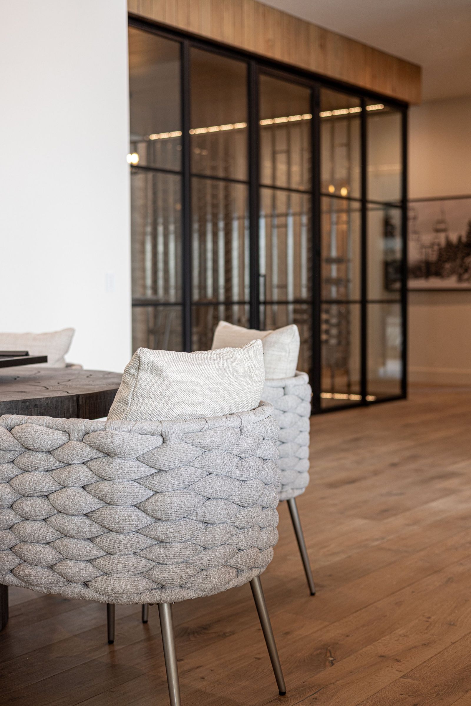 Woven lounge chair beside a steel-and-glass wine room