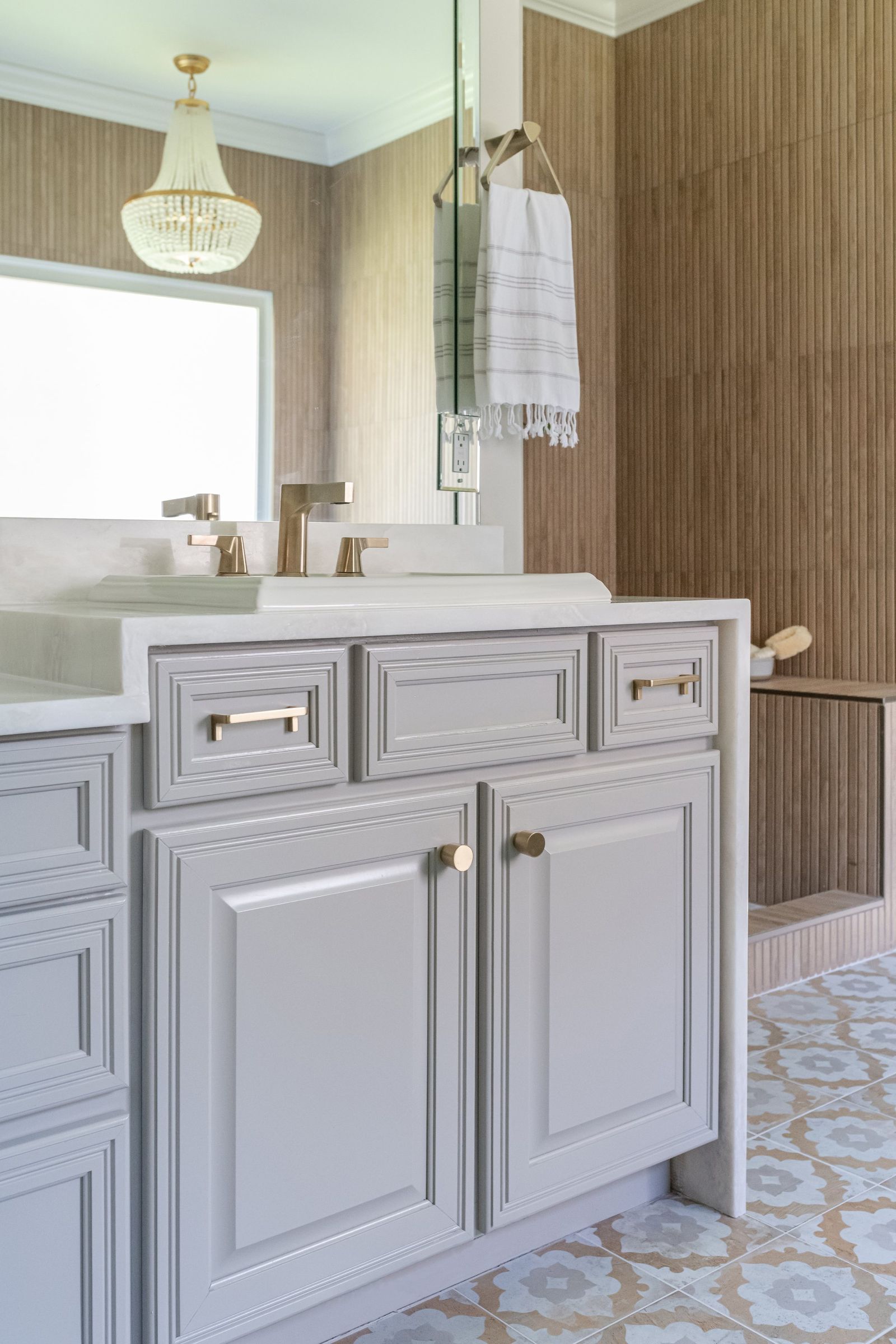 Beaded chandelier over the tub seen past a grey vanity with brass hardware