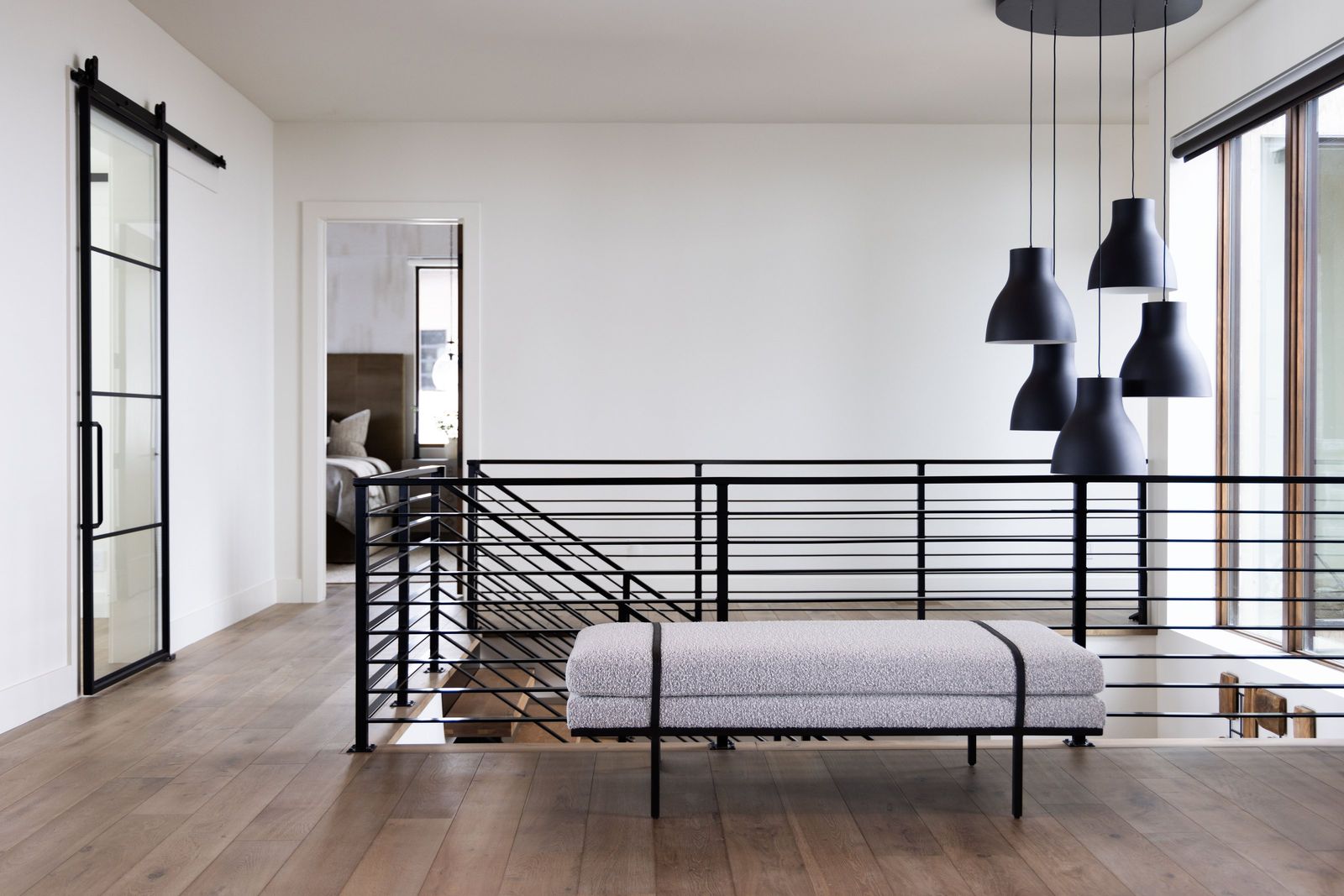 Upper landing with black cluster pendants, a steel-framed glass barn door and a horizontal rail
