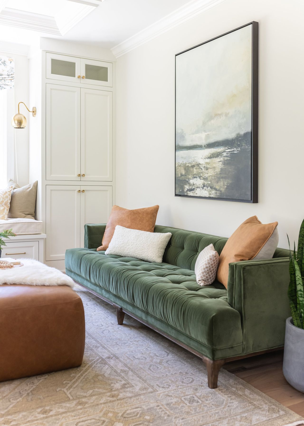Tufted green velvet sofa with rust and ivory pillows beneath a large abstract landscape
