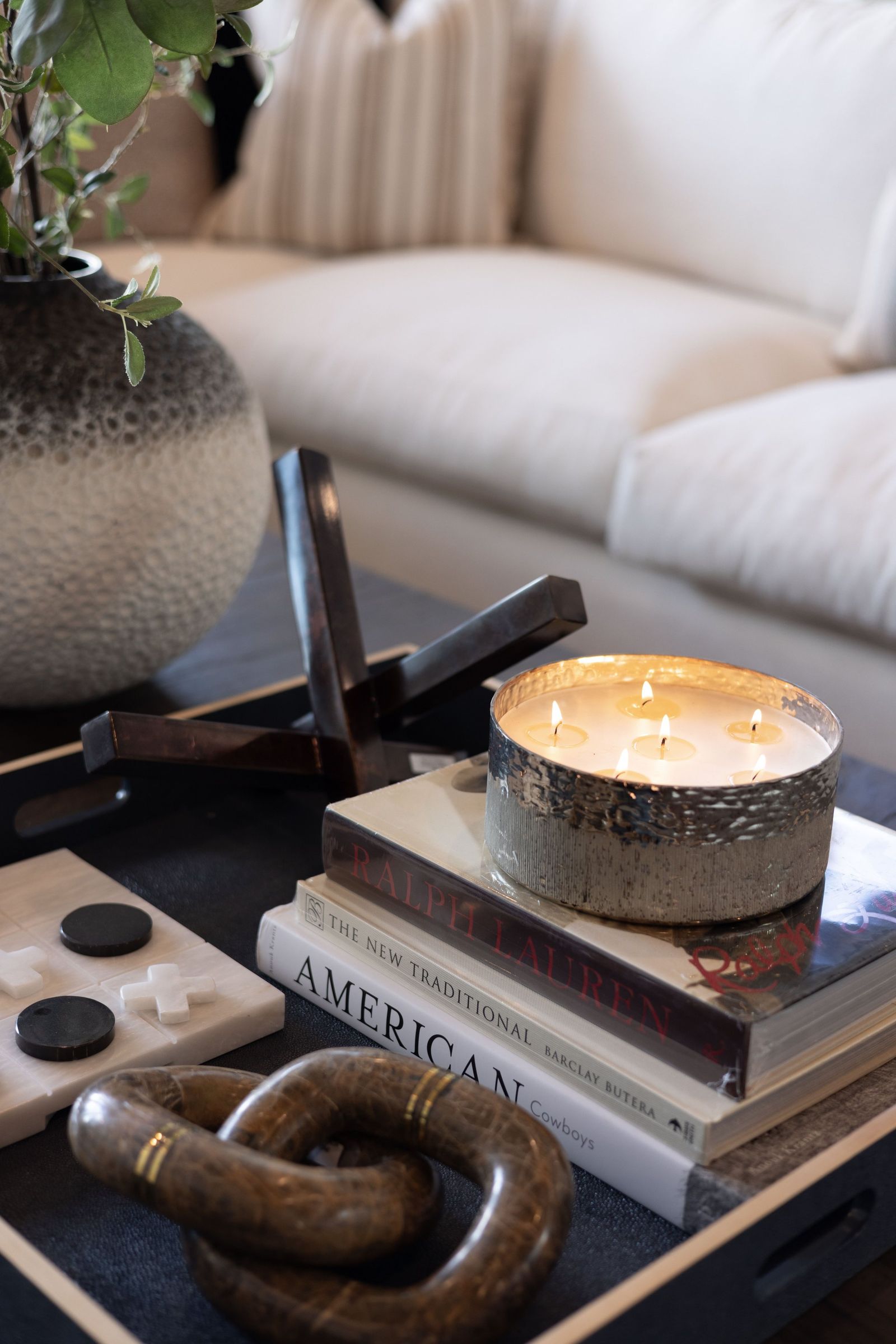 Coffee table vignette with a lit candle, stacked books and a carved wood chain link