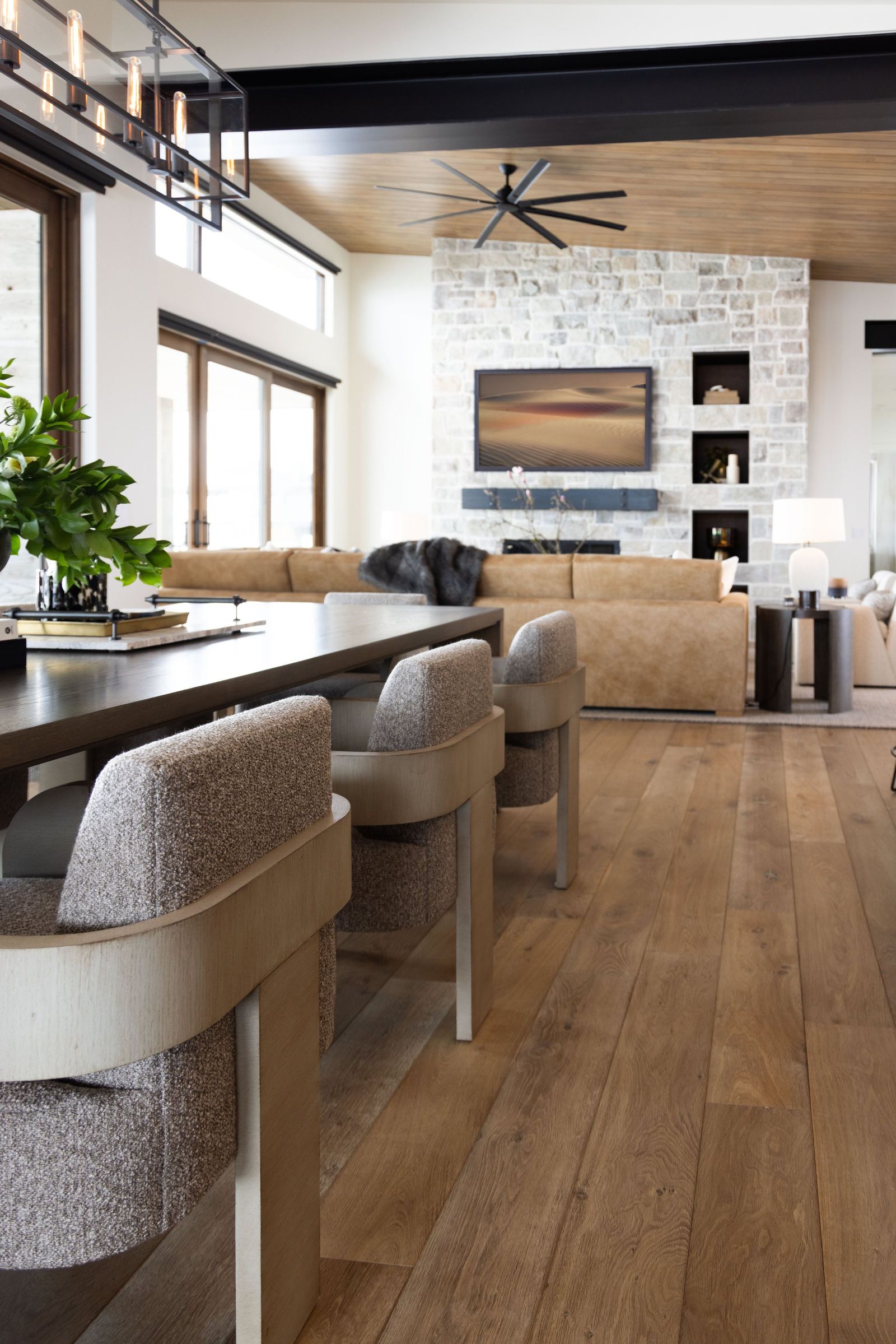 Dining table with boucle and oak chairs looking across the great room to the stone fireplace
