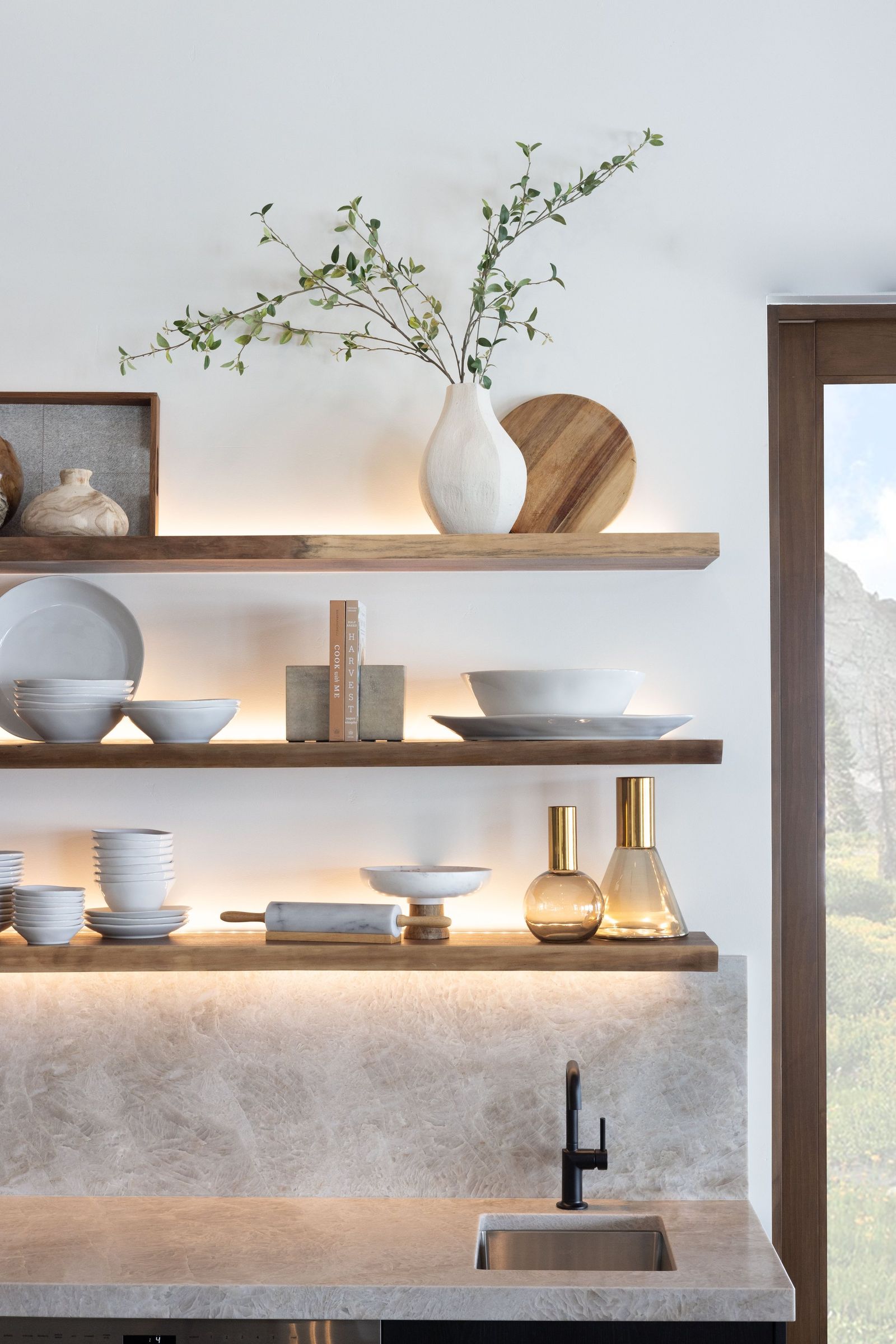 Lit walnut floating shelves with white ceramics and brass pieces above a quartzite backsplash