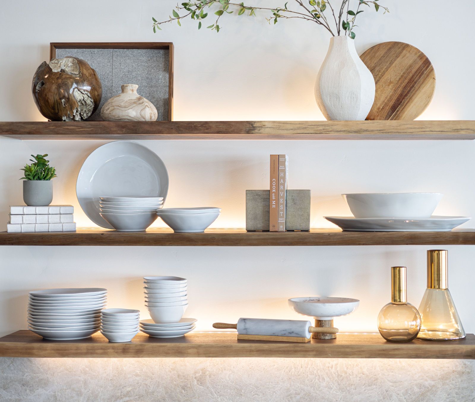 Backlit walnut shelves styled with stoneware, wood boards and a white bud vase