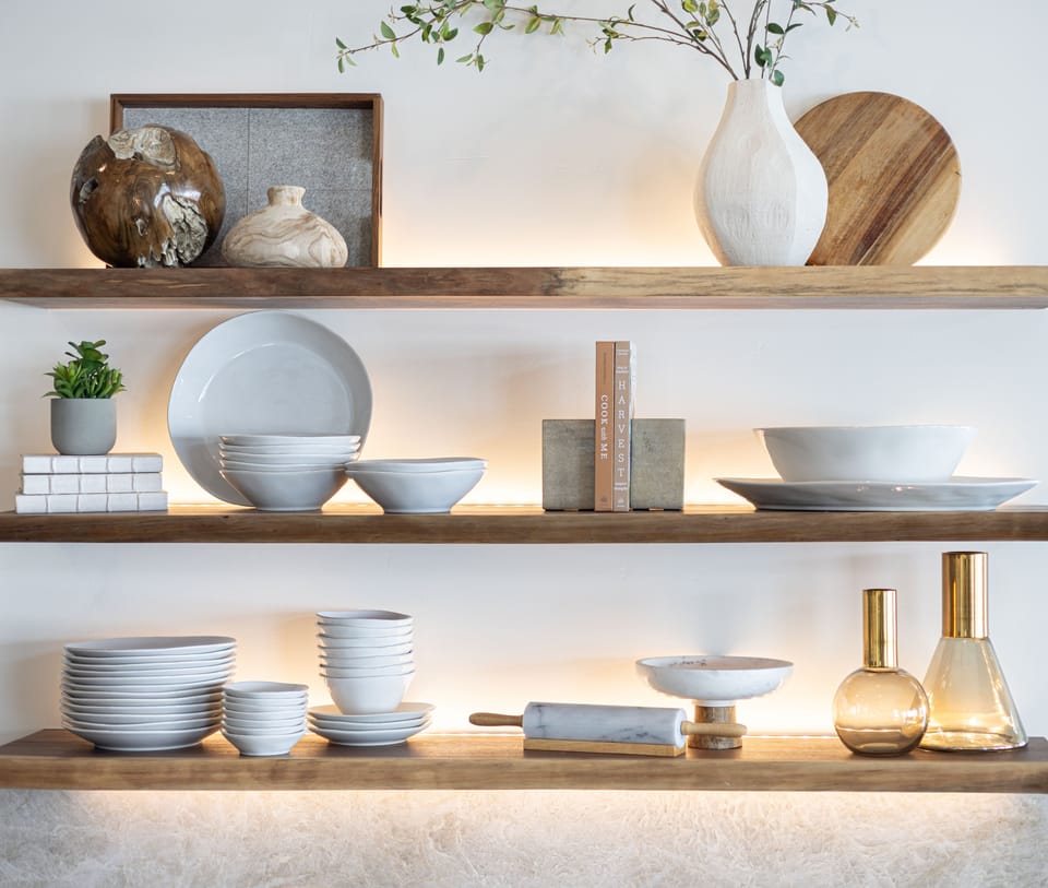 Backlit walnut shelves styled with stoneware, wood boards and a white bud vase