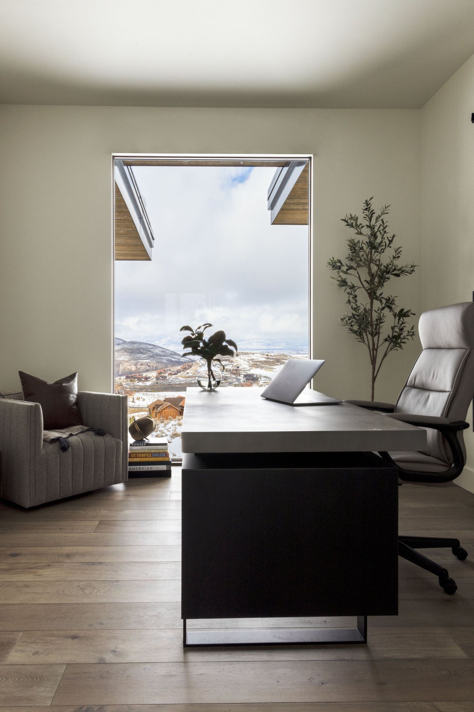 Home office with a dark desk and leather chair facing a picture window of snowy hills