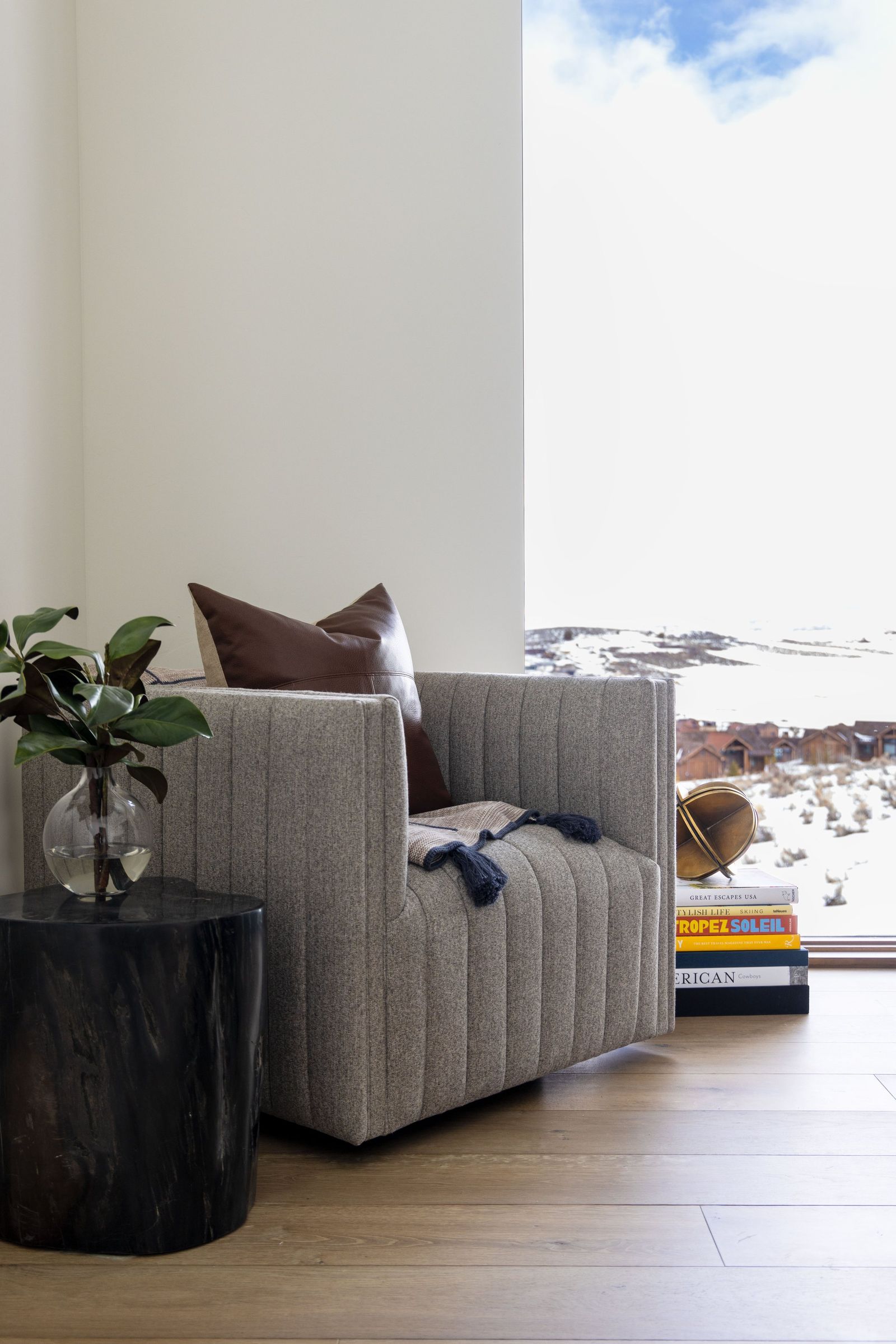 Channel-tufted reading chair beside a tall window with snow-covered mountain views