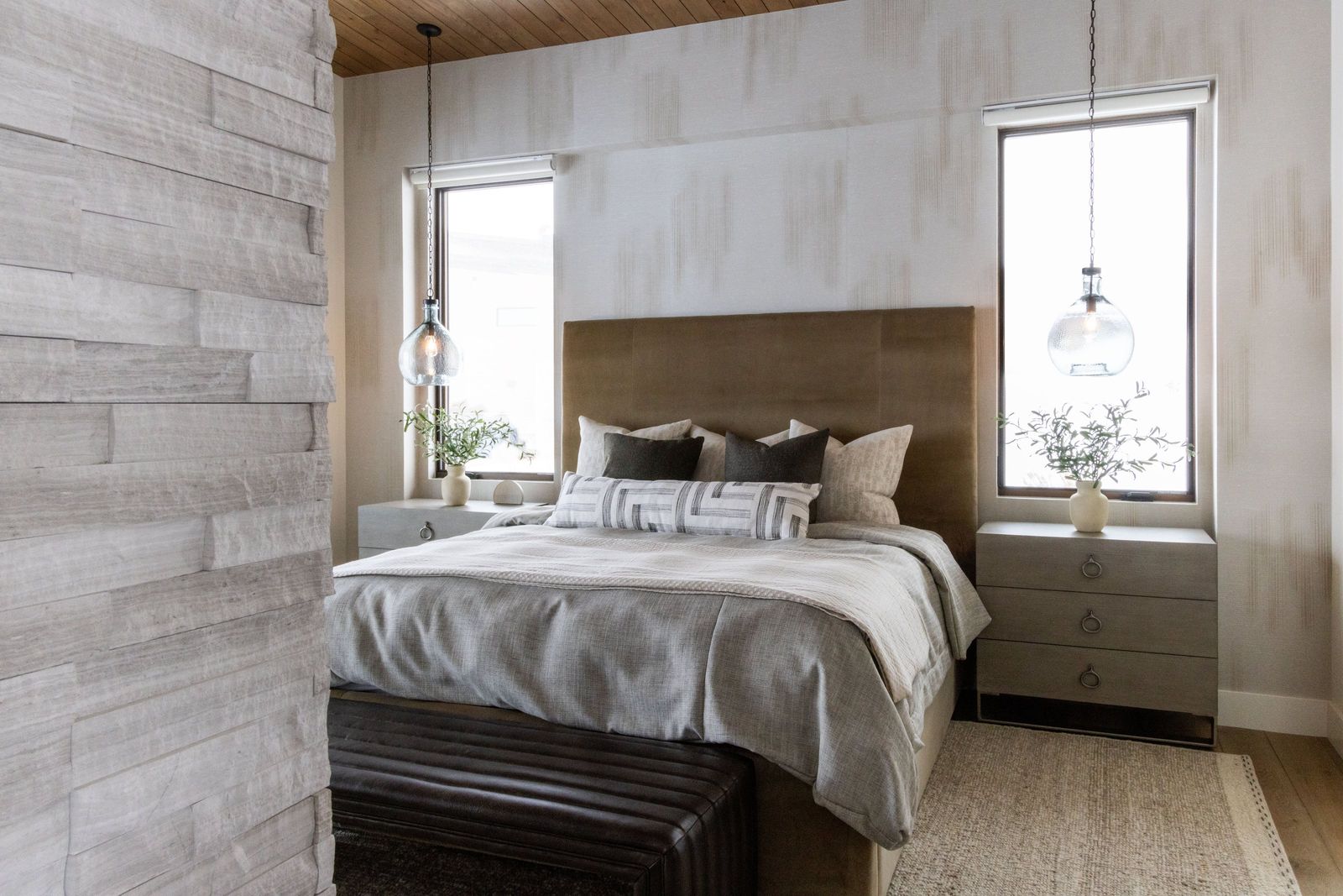 Primary bedroom with a tall bronze upholstered headboard, layered linens and glass pendants