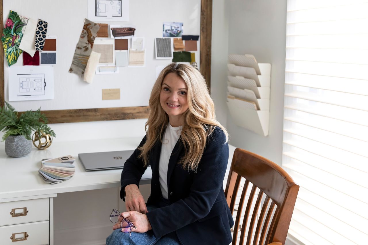 Joni Glass at her desk with fabric samples and a pinned design board behind her
