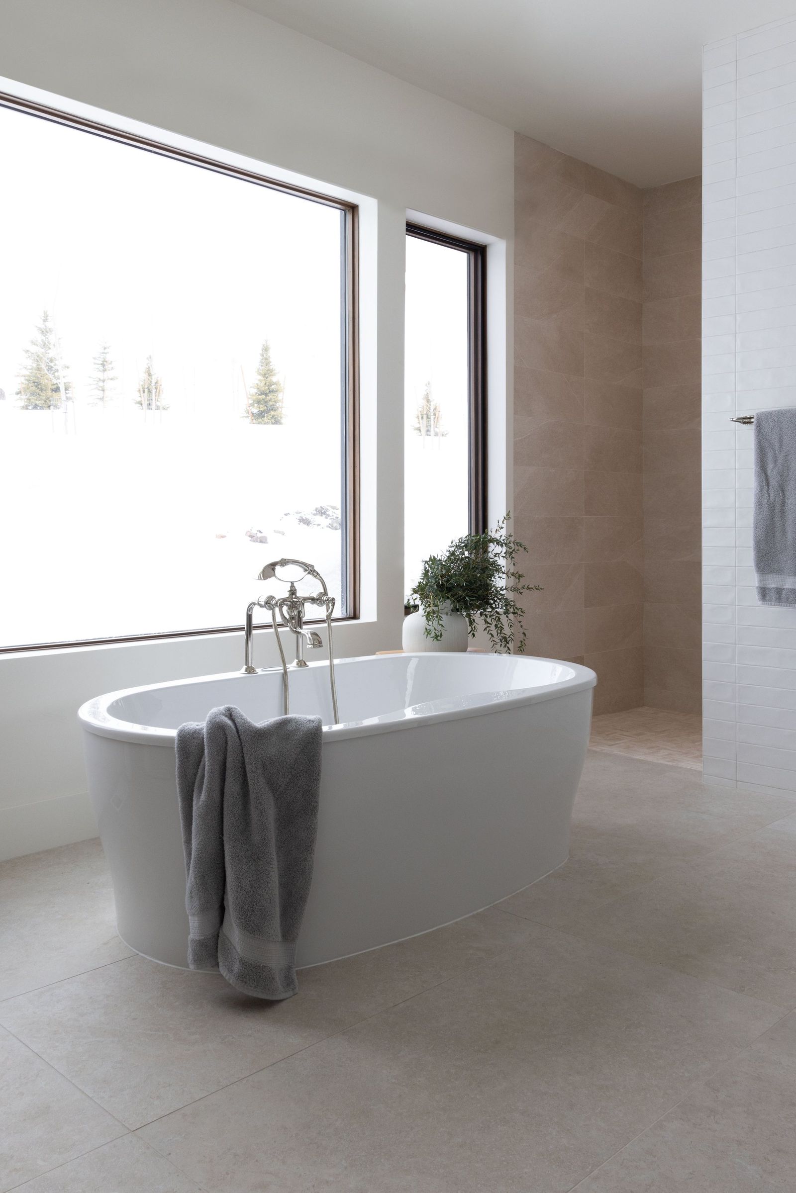 Freestanding soaking tub beneath a tall window in a calm, tone-on-tone primary bath