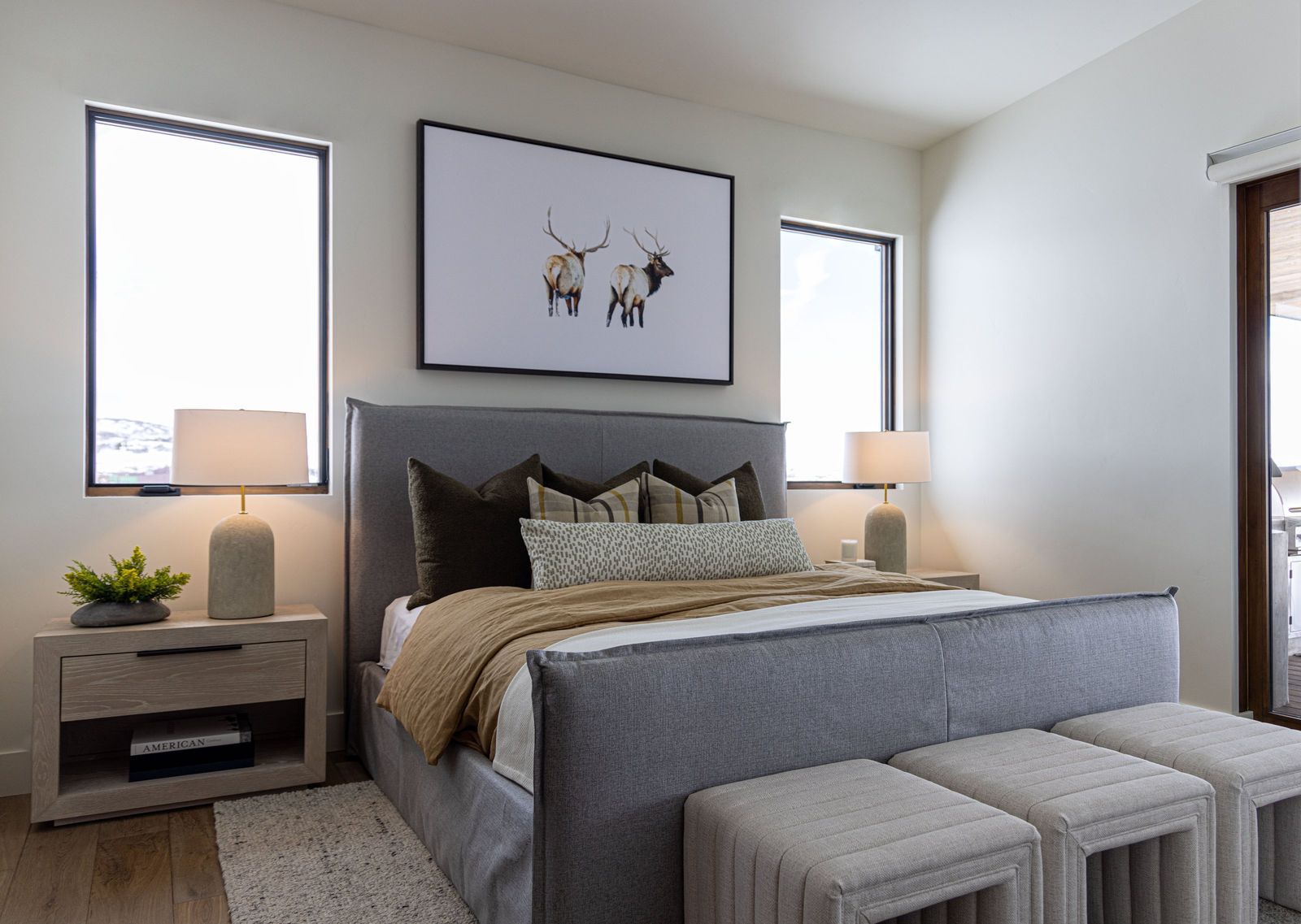 Second primary suite with a grey upholstered bed, elk art print and linen-shaded lamps
