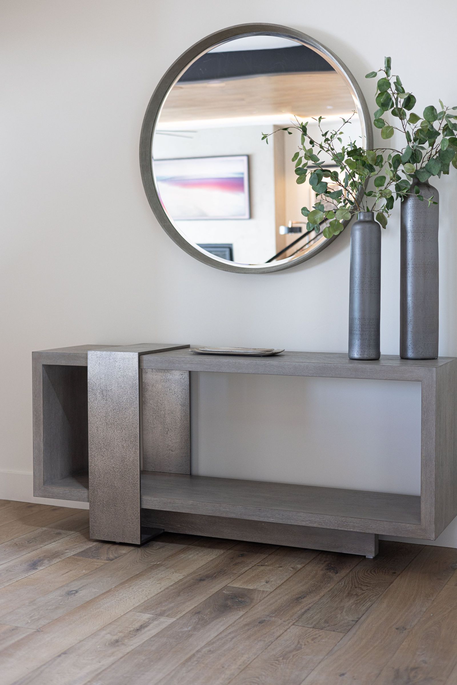 Sculptural concrete console under a round mirror with tall grey vases and eucalyptus