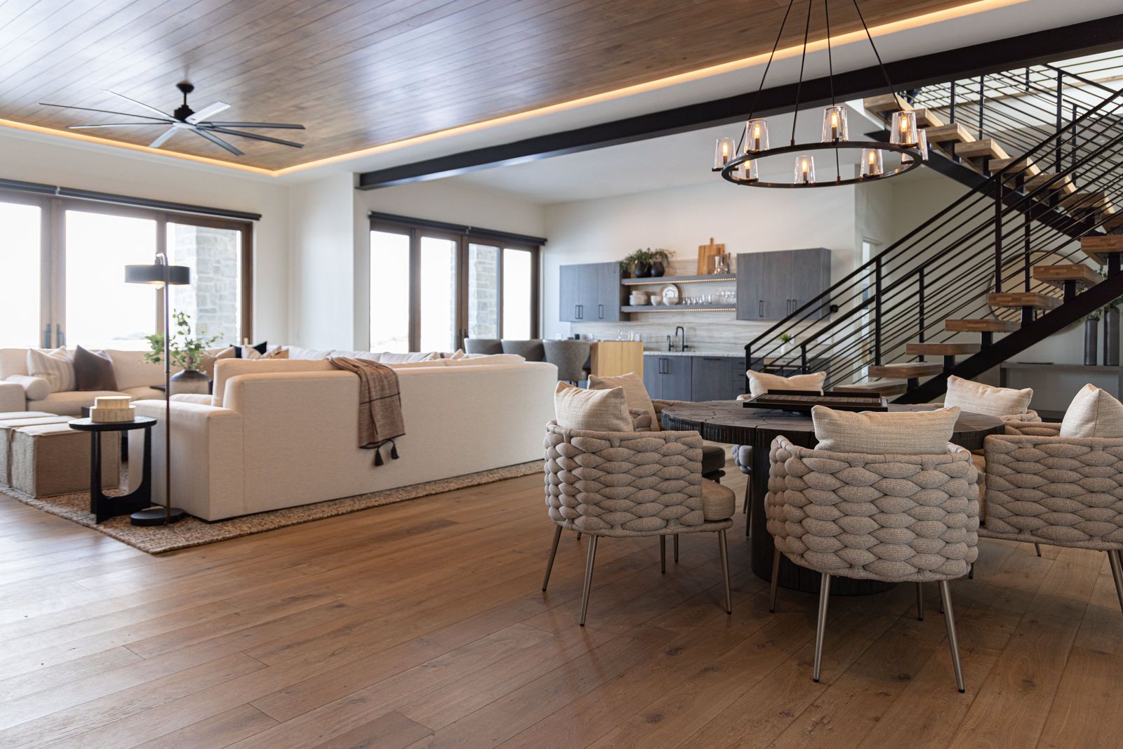 Lower-level family room with woven chairs, a candle chandelier and a floating staircase