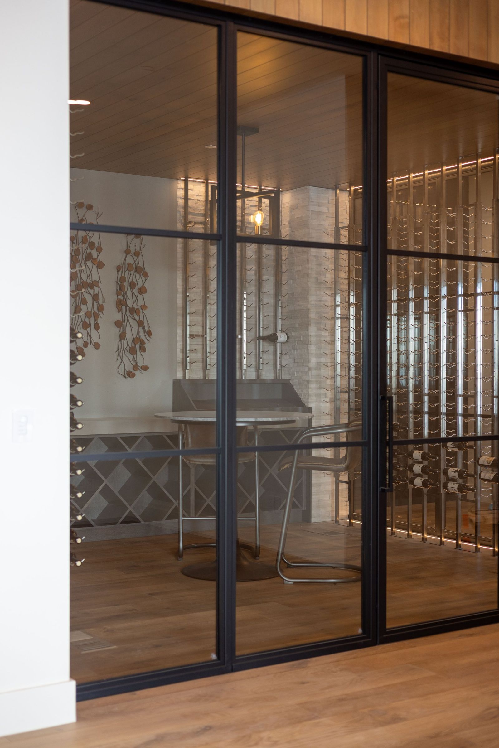 Steel-framed glass wine room with backlit racks and a tasting table