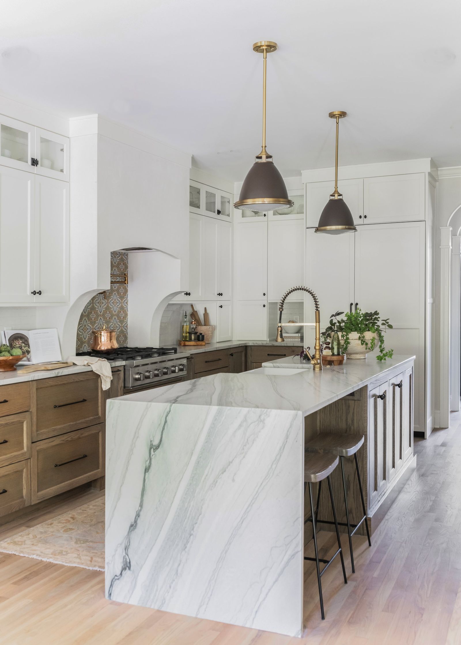 White and oak kitchen with a veined quartzite waterfall island and bronze dome pendants