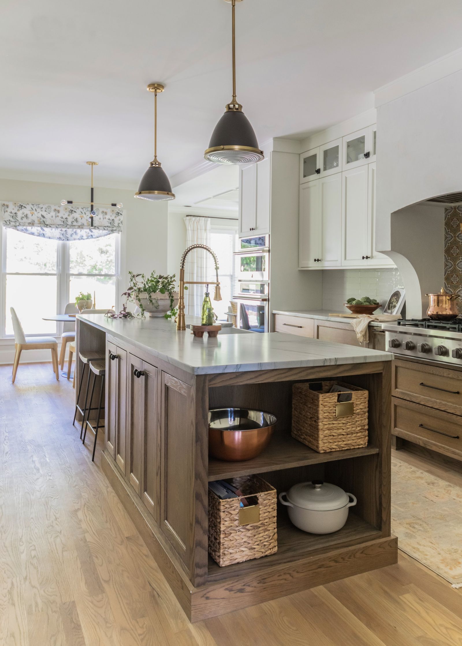Oak island with open shelves, woven baskets and a Dutch oven, looking to the breakfast nook