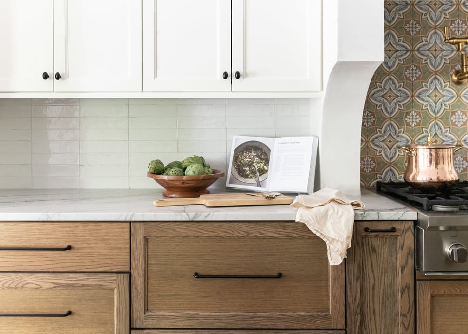 Oak drawers, marble counter and a copper pot beside the patterned tile range alcove