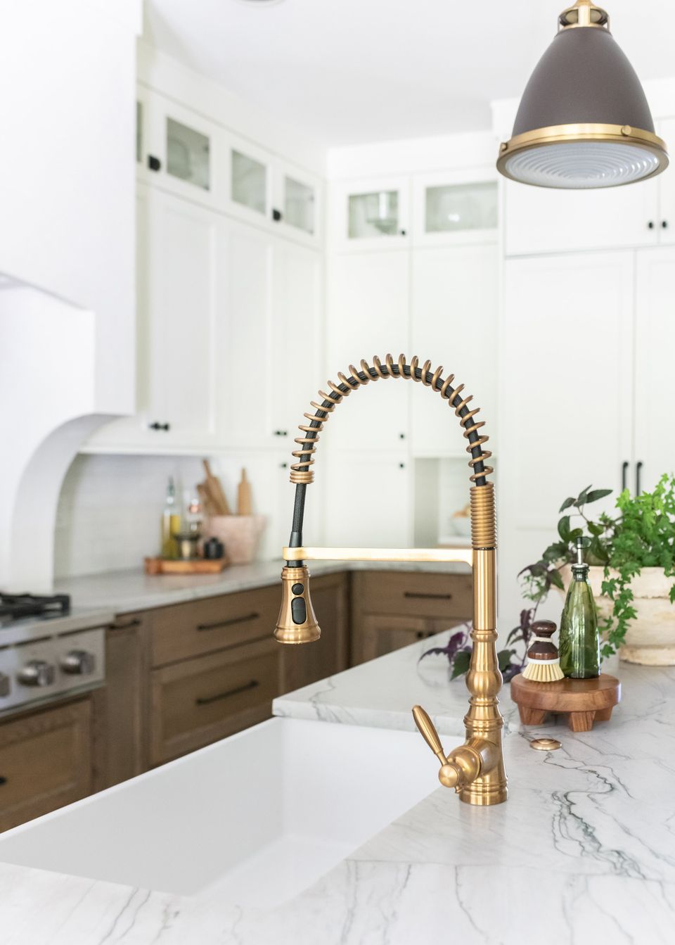 Brass spring faucet over a white farmhouse sink with marble counters