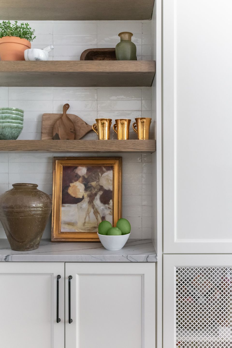 Walnut open shelves styled with brass cups, pottery and a framed floral painting