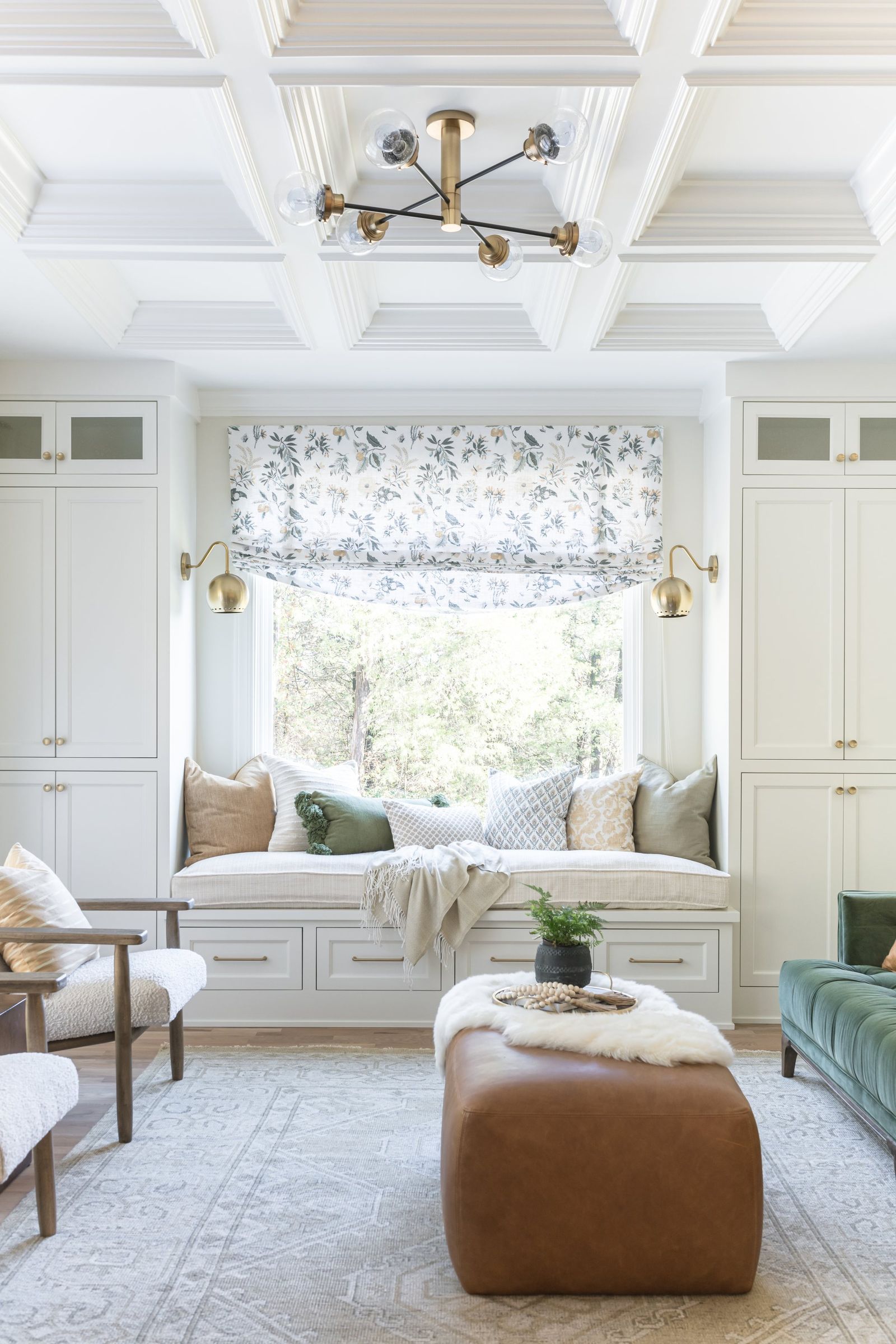 Coffered ceiling and brass chandelier above a built-in window seat flanked by cabinets