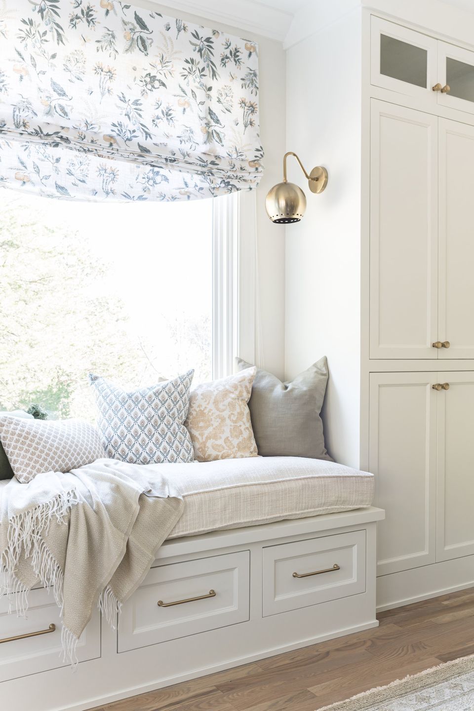 Built-in window seat with ivory cushions, patterned pillows and a brass swing-arm sconce