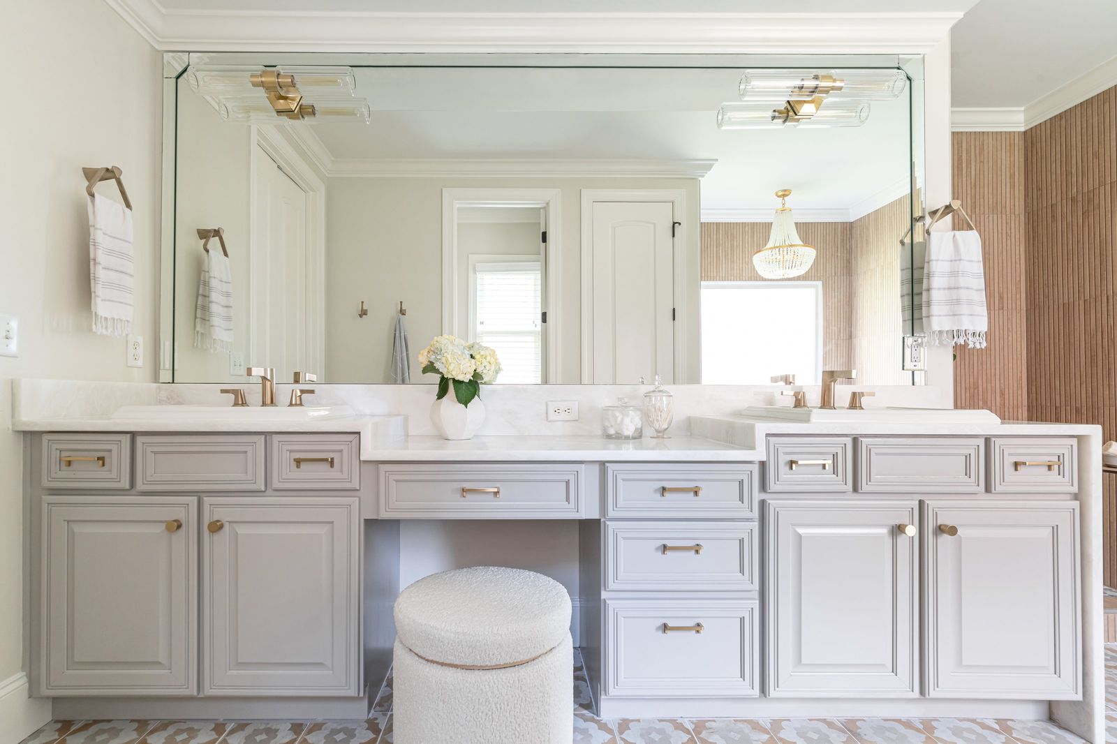Double vanity in warm grey with a makeup counter, brass pulls and patterned cement tile