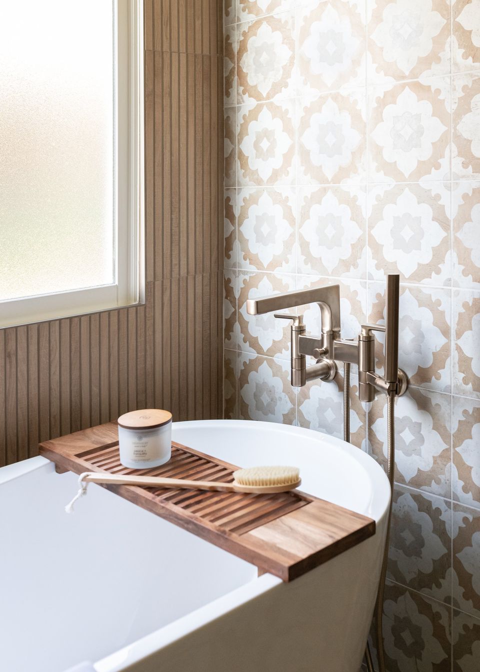 Wood bath caddy and brushed brass tub filler against patterned tile