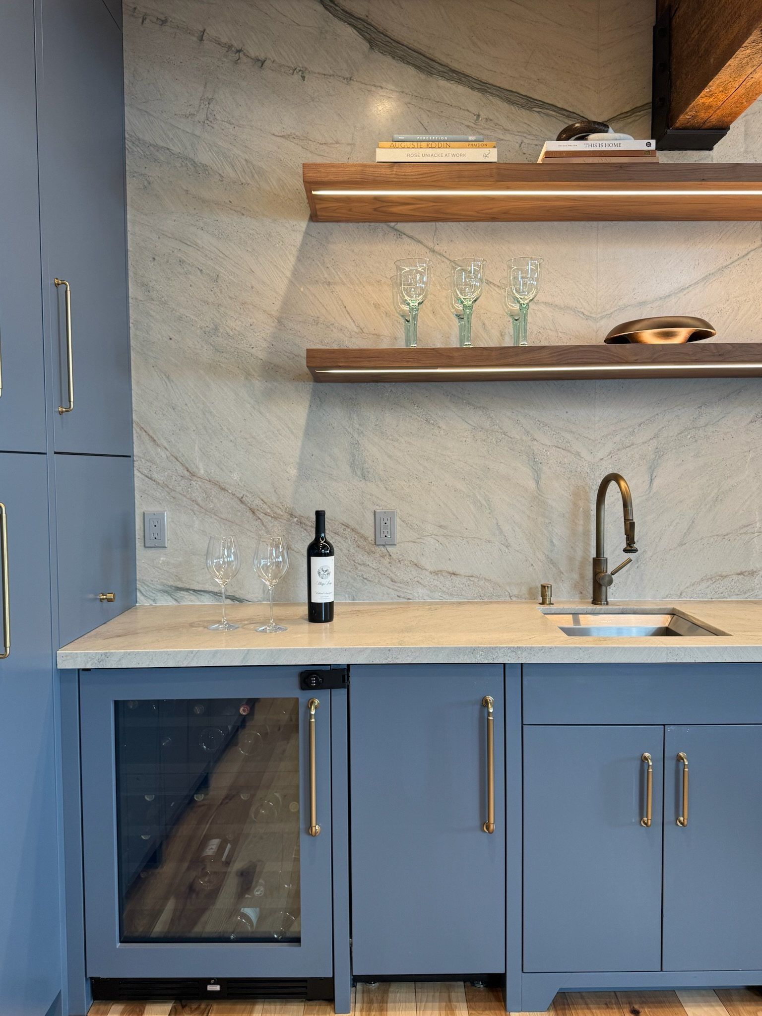 Blue wet bar with a wine fridge, walnut floating shelves and a full-height quartzite slab