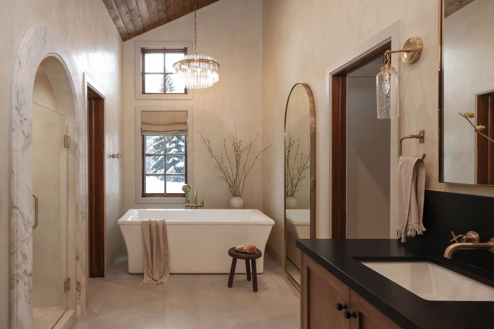 Plaster primary bath with a crystal chandelier, freestanding tub and marble-arched shower