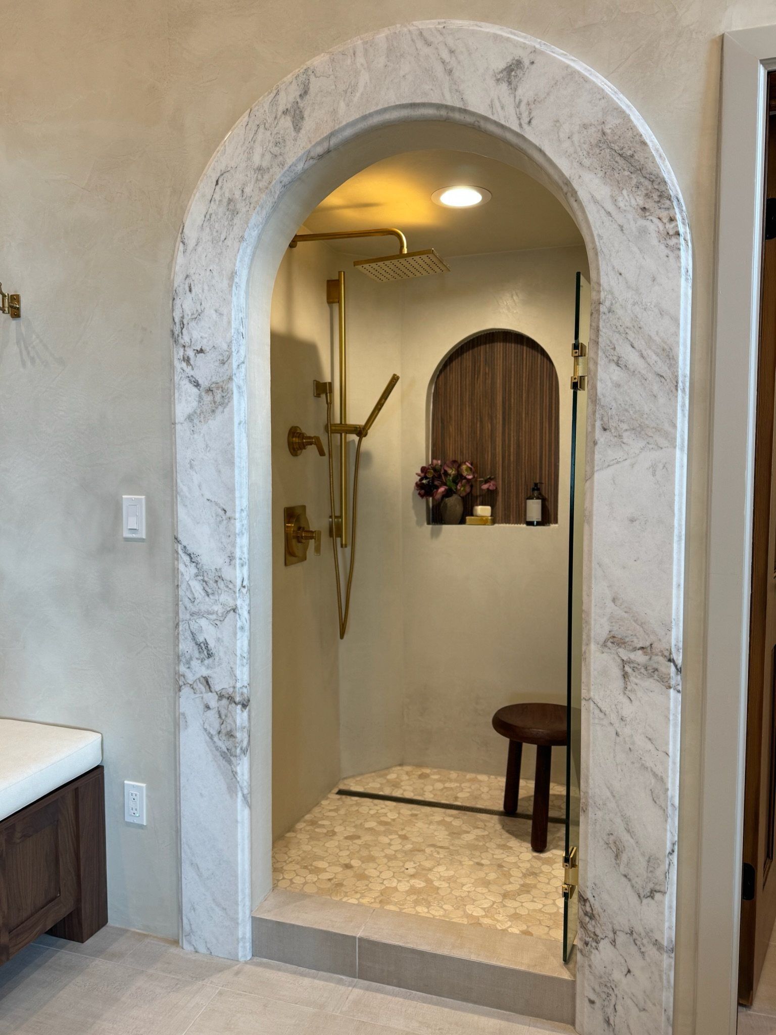 Marble-arched shower entry with a wood-lined niche and brass fixtures