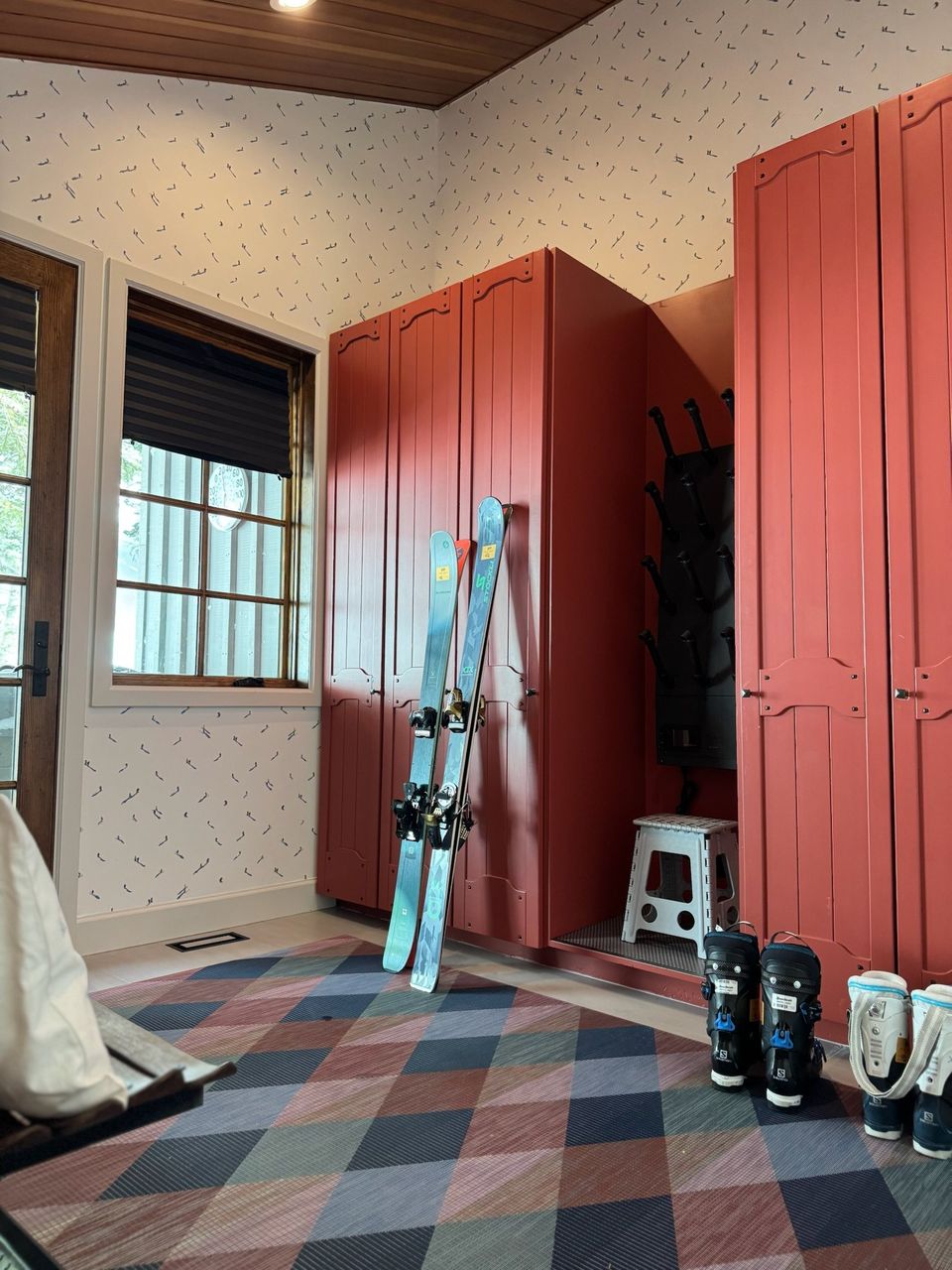 Ski room with coral-red lockers, a plaid carpet and skis by the window