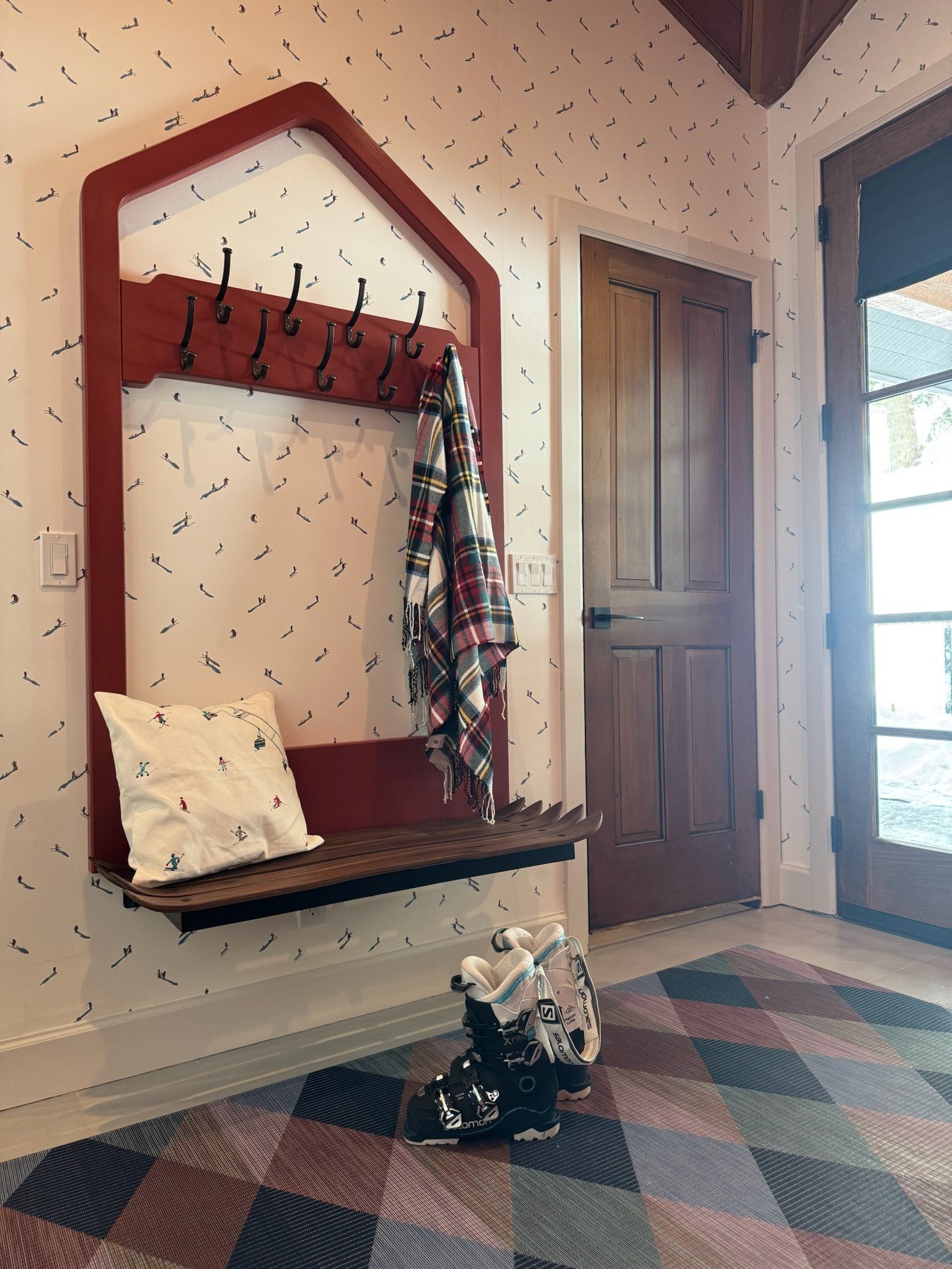 Chalet-shaped red coat rack and bench with a plaid scarf and ski boots