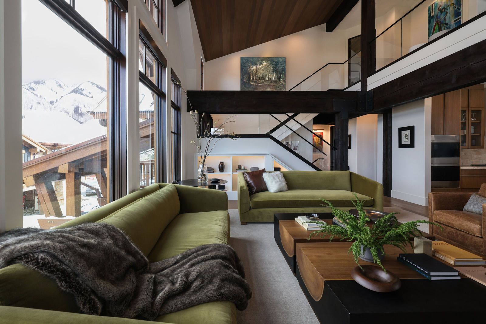 Great room with olive velvet sofas and a live-edge coffee table below windows to snowy peaks