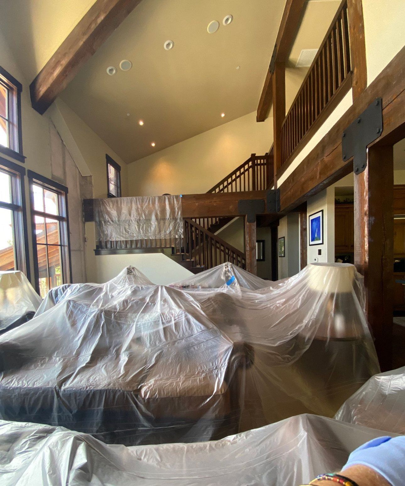 Before: Ross great room after: olive velvet sofas, timber beams, and tall windows toward the loft and stair