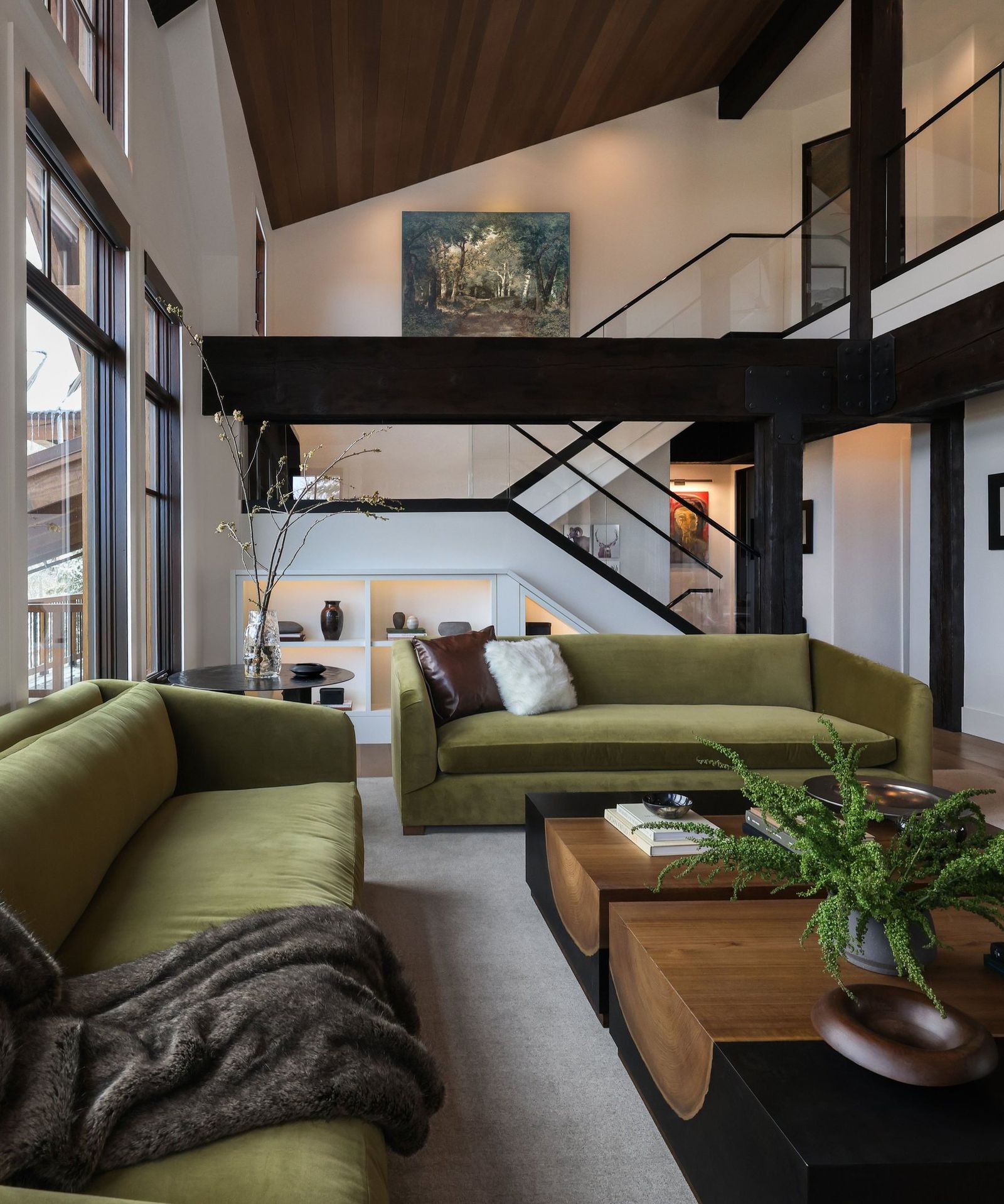 Ross great room after: olive velvet sofas, timber beams, and tall windows toward the loft and stair