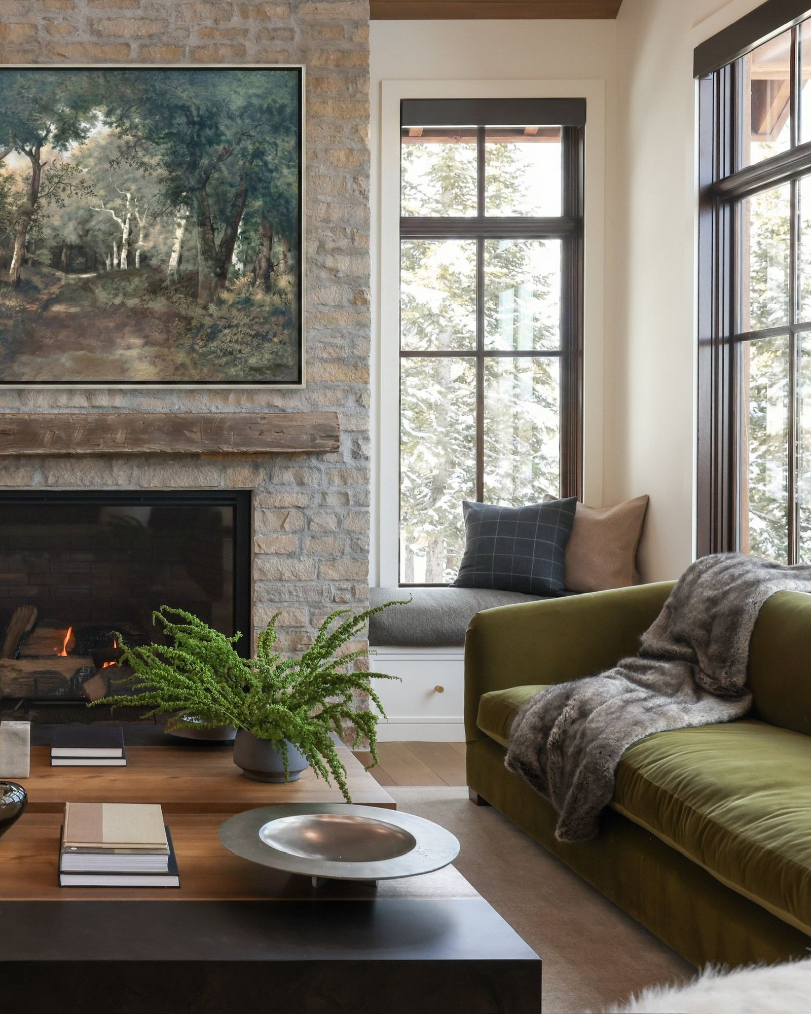 Stacked-stone fireplace with a forest painting, olive sofa and a fern on the coffee table