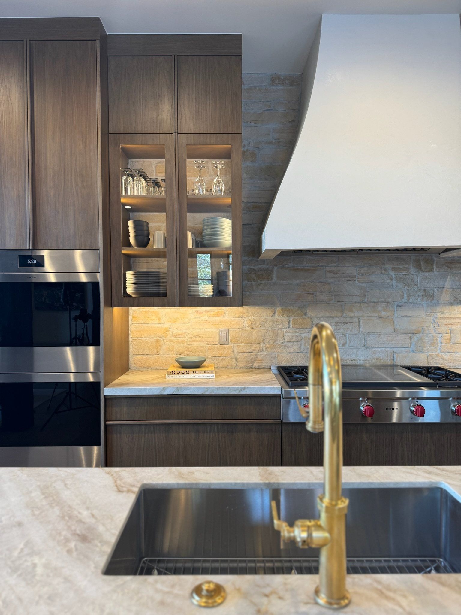 Brass faucet at the island with glass-front walnut cabinets and the plaster hood beyond
