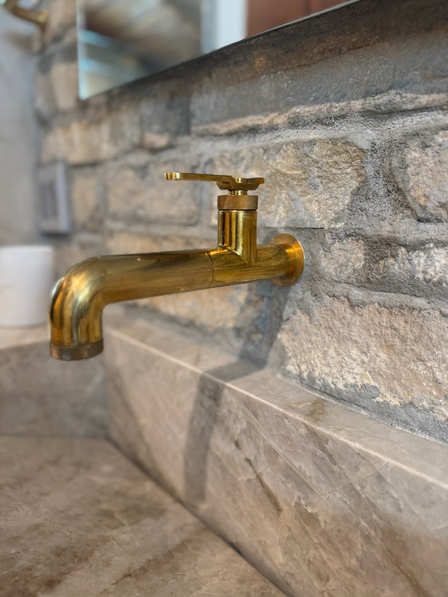 Brass wall-mount spout against rough-cut stone