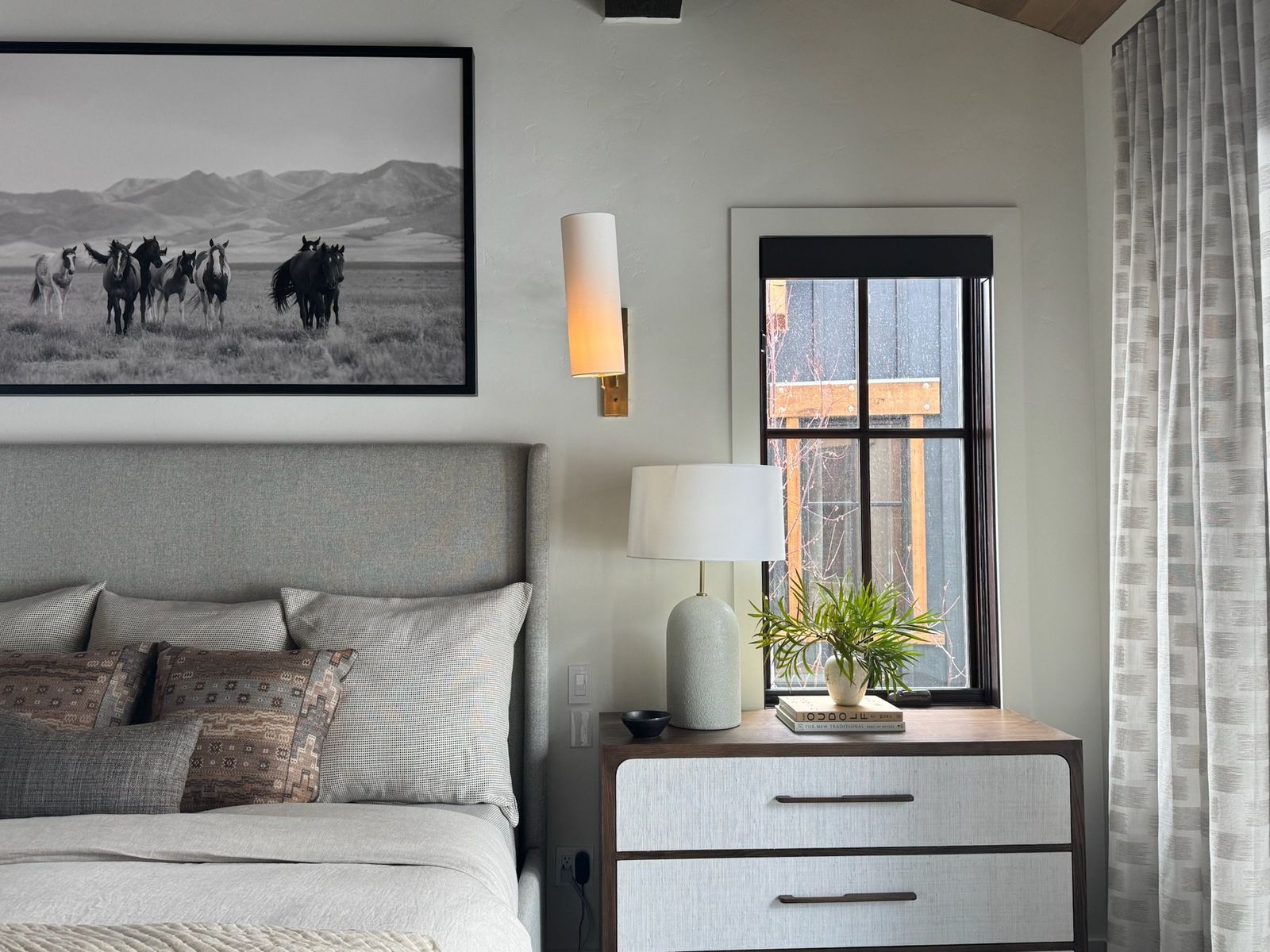 Bedside with a white lacquer chest, ceramic lamp and brass sconce under the horse print