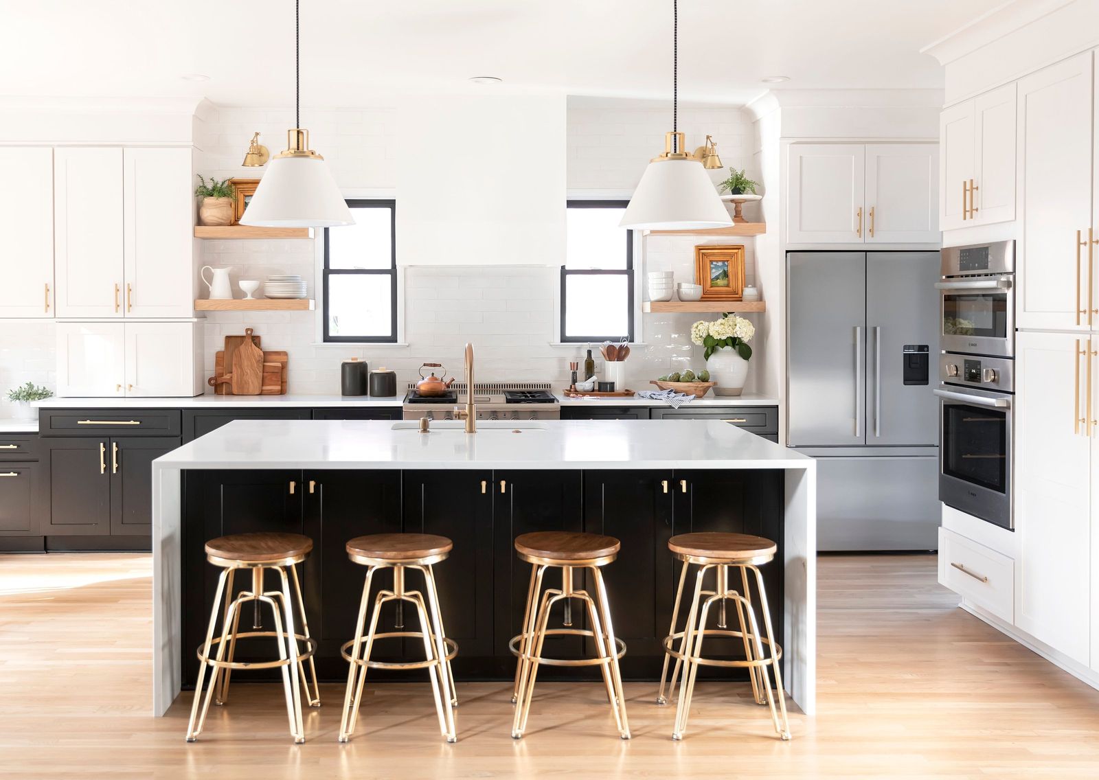 White kitchen with a black waterfall island, brass stools and white oak open shelves