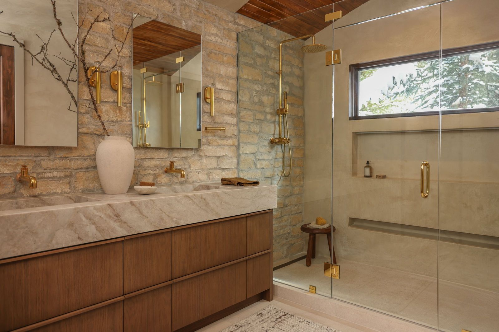 Primary bath with a stone wall, walnut vanity, brass fixtures and a glass steam shower