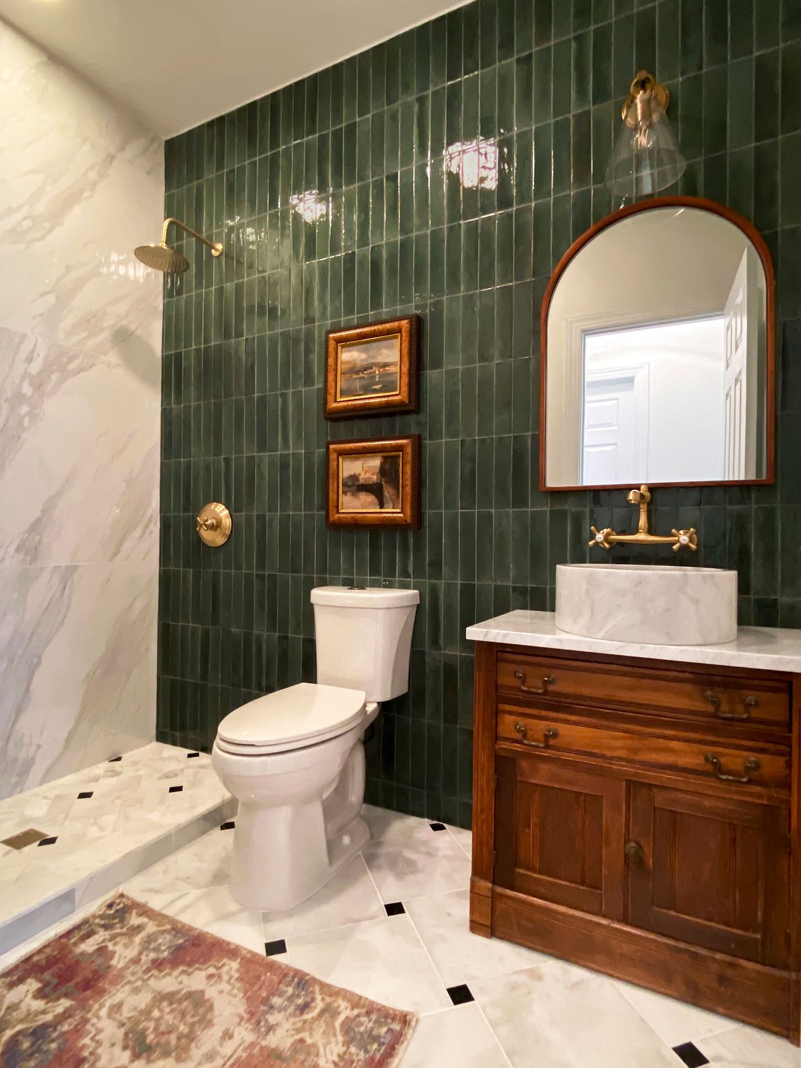 Powder bath with green zellige tile, an antique wood vanity and an arched brass mirror