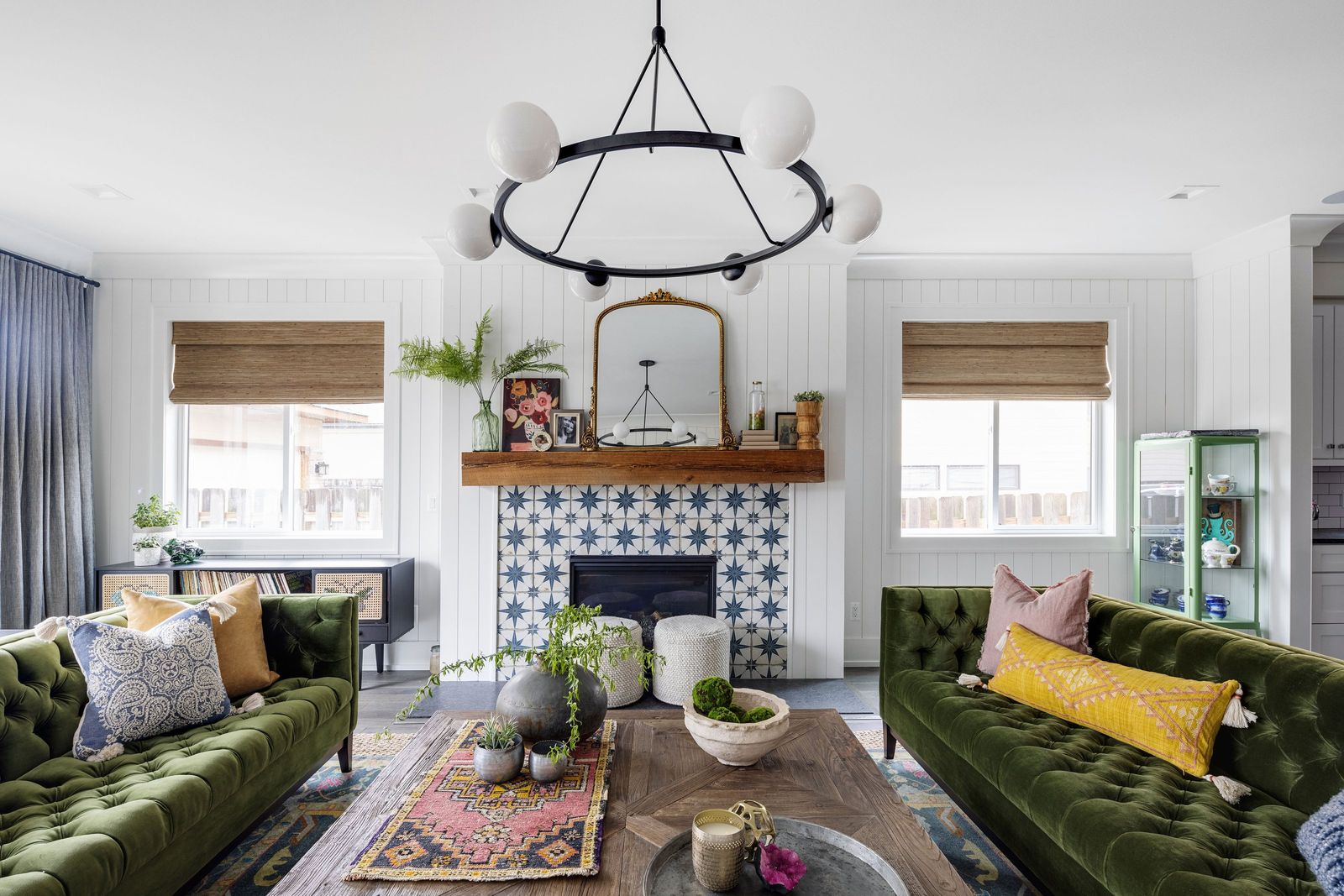 Eclectic living room with green velvet sofas, a blue patterned tile fireplace and ring chandelier