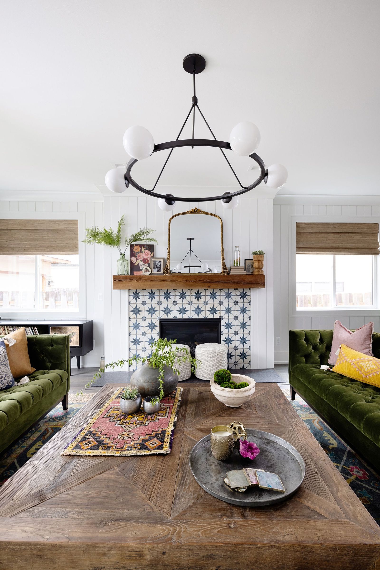 Ring chandelier over a wood coffee table with the tiled fireplace and gilt mirror beyond