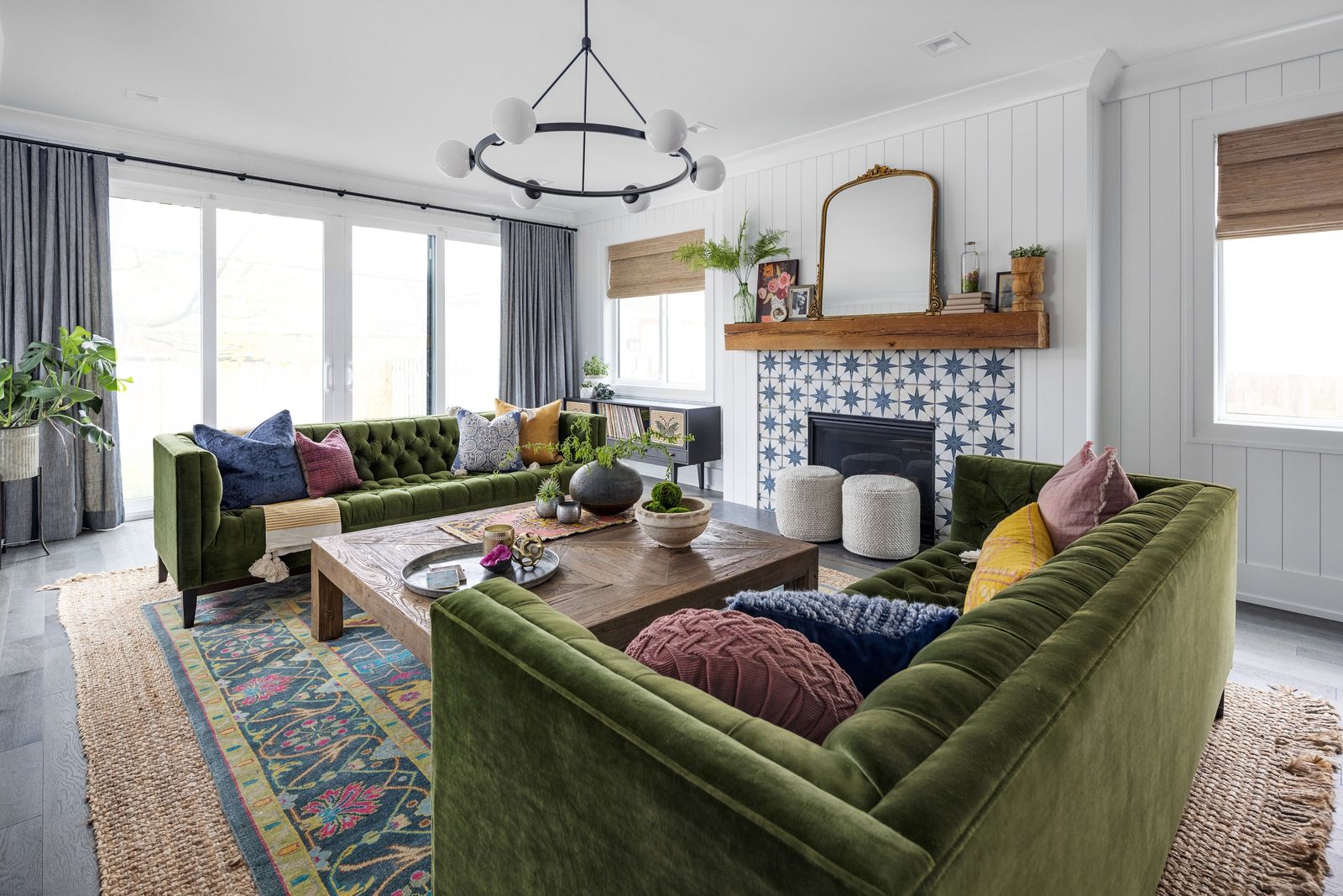 Green velvet sectional with colorful pillows on a layered rug in a bright living room