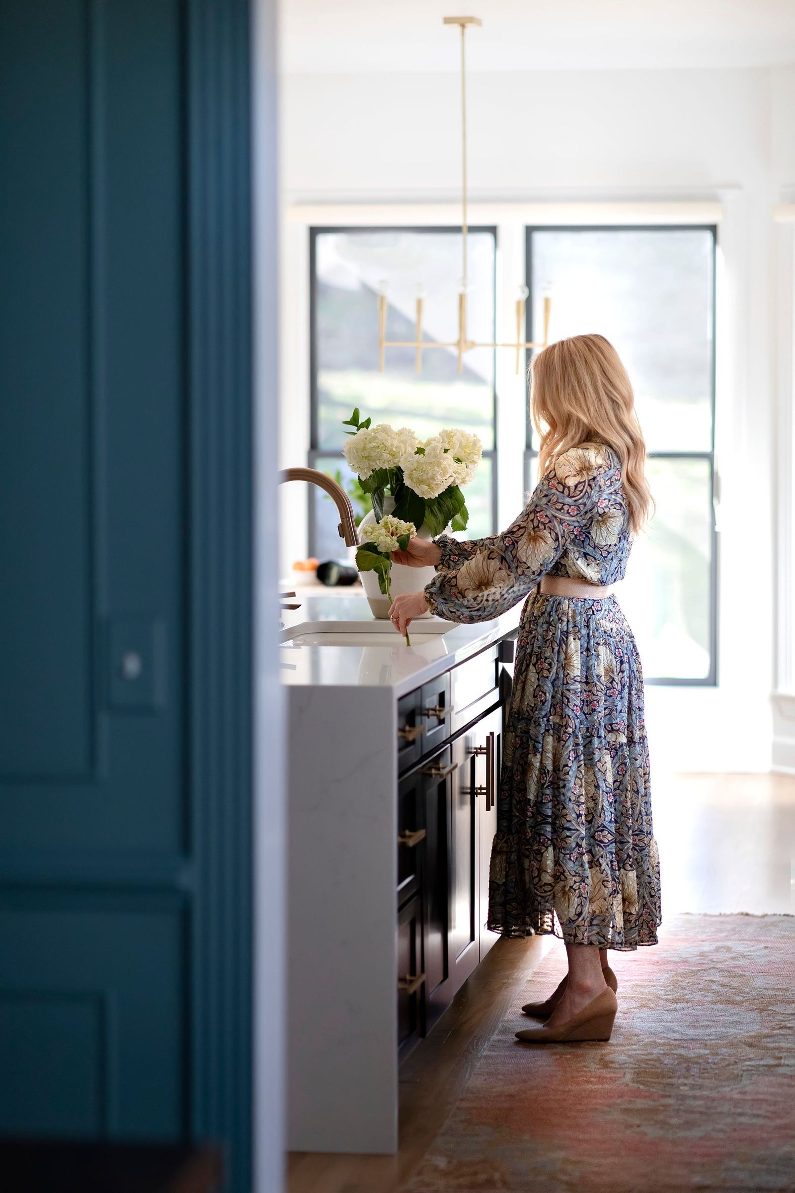 Joni Glass arranging white hydrangeas in a bright kitchen, framed by a teal door