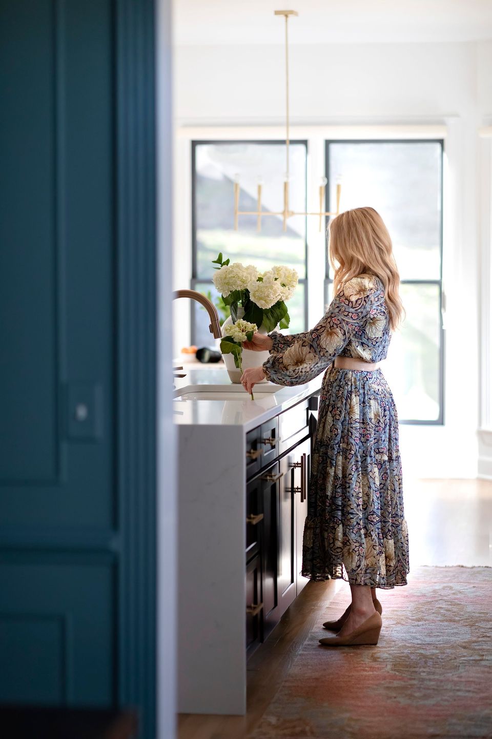Joni Glass arranging white hydrangeas in a bright kitchen, framed by a teal door