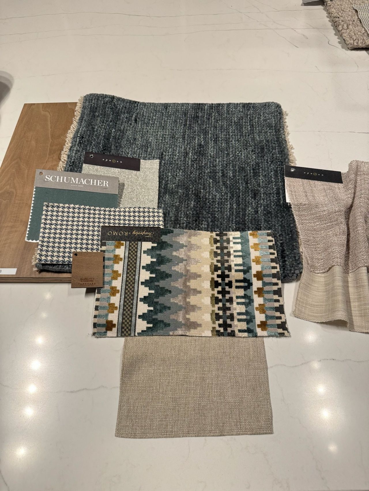 Fabric samples laid out on a counter: slate wool, houndstooth, a teal geometric weave and linen