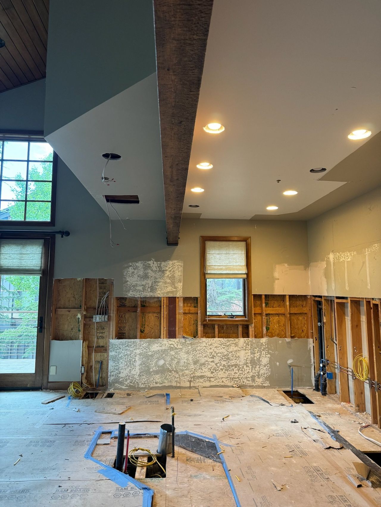 Kitchen stripped to the studs under a timber beam, with plumbing roughed in and the floor papered